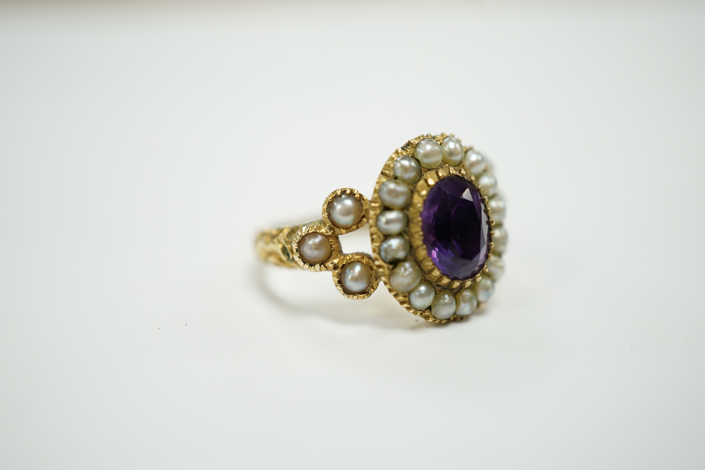 A Victorian yellow metal seed pearl and amethyst set oval cluster ring, size L, gross weight 3.7 grams.